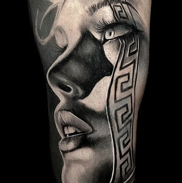 Close-up of a woman's face featuring a black and grey tattoo design.