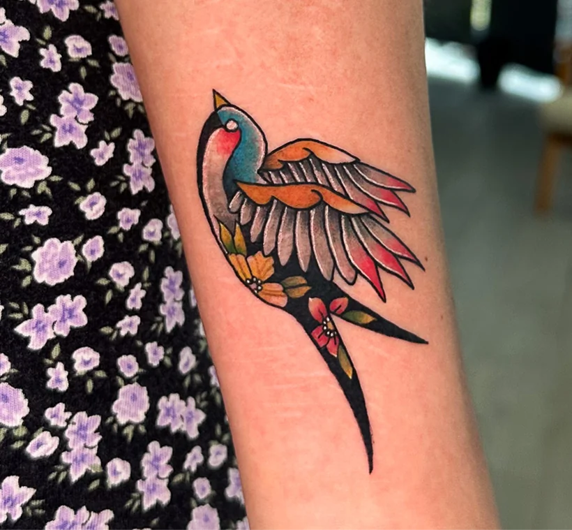 A traditional style color tattoo on a forearm, depicting a flying swallow.