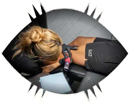 Professional tattoo artist wearing black gloves carefully inking a flash tattoo design on a client's leg during a studio session.