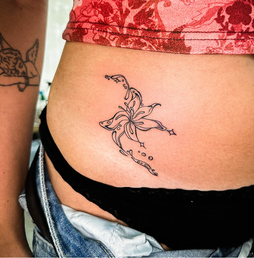 Delicate fine line black ink tattoo on a person's hip, featuring an abstract, geometric floral design.