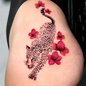 Blackwork tattoo of a prowling leopard surrounded by vibrant red color realism flowers on a hip.