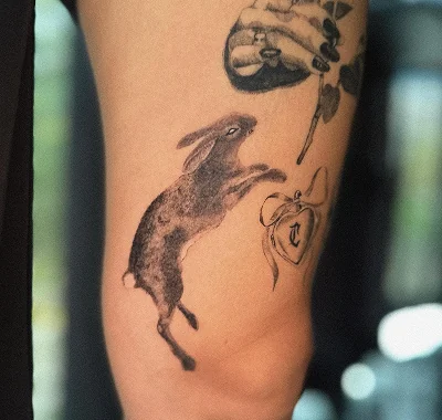 Medium black and grey custom tattoo showing a beautifully textured leaping rabbit placed near a heart locket.