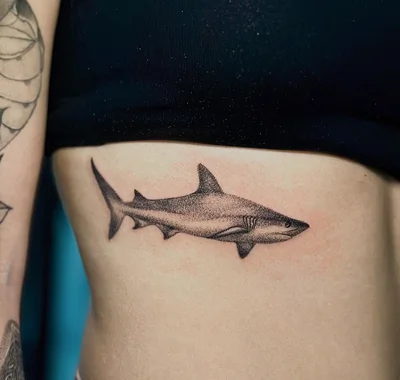 Highly detailed small black and grey custom tattoo of a shark on a person's ribcage, showcasing intricate dotwork and smooth shading techniques to create a realistic texture.
