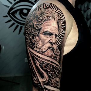 Blackwork realism tattoo on a shoulder featuring a portrait of a bearded Greek god with a trident and a Greek key halo.