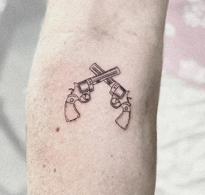 Highly detailed minimalist fine line tattoo featuring two crossed vintage revolvers, enhanced with delicate dotwork shading on a person's arm.